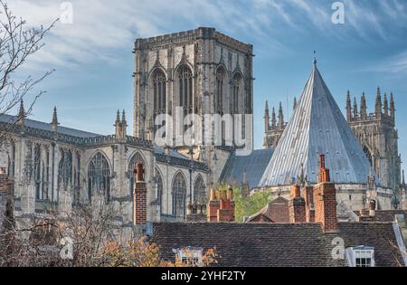 Die Türme des York Minster, von den Dächern einiger historischer Gebäude aus gesehen. Im Vordergrund stehen Bäume und ein Himmel mit Wolken. Stockfoto