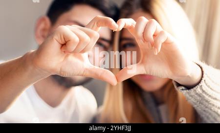 Liebevolle junge Zweierfamilie, die sich zuhause mit den Fingern Herz macht, konzentrieren sich auf die Hände Stockfoto