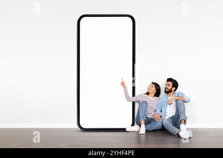 Ein Paar genießt die gemeinsame Zeit neben einem großen leeren Smartphone-Display im Innenbereich Stockfoto