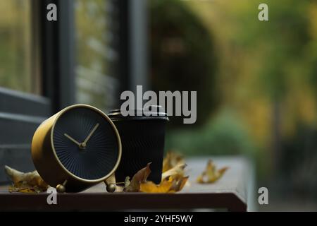 Herbstzeit. Wecker, gefallene Blätter und Tasse mit heißem Getränk in der Nähe des Cafés im Freien, Platz für Text Stockfoto