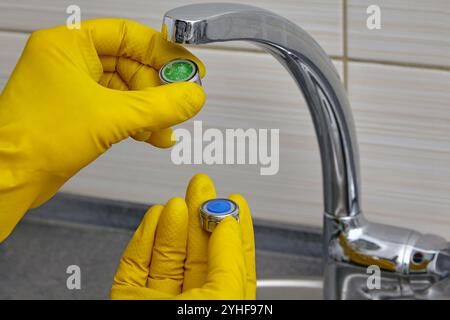 Ersetzen eines verstopften Wasserhahnbelüfters durch einen neuen. Klempner in gelben Gummihandschuhen mit Belüfter Stockfoto