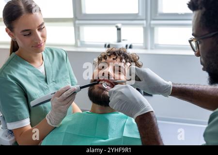 Männlicher Zahnarzt, der die Zähne des Patienten während der Untersuchung in der zahnärztlichen Praxis mit kieferorthopädischen Werkzeugen untersucht Stockfoto
