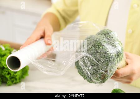 Frau, die Plastikfolie über Brokkoli auf der Arbeitsplatte in der Küche legt, Nahaufnahme Stockfoto