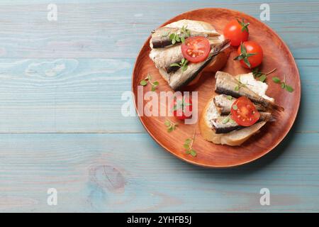 Köstliche Sandwiches mit Sprotten, Mikrogrün und Tomaten auf hellblauem Holztisch, Blick von oben. Leerzeichen für Text Stockfoto