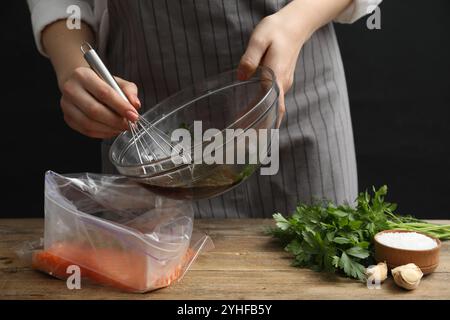 Frau mit Sojamarinade und Lachsfilet in Plastiktüte am Holztisch, Nahaufnahme Stockfoto