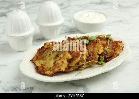 Köstliche Kartoffelpfannkuchen mit frischem Mikrogrün und Sauerrahm auf weißem Marmortisch, Nahaufnahme Stockfoto