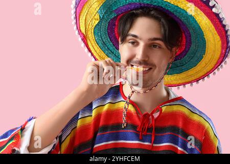 Junger mexikanischer Mann isst Nachos auf rosa Hintergrund Stockfoto