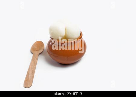 Ein traditionelles indisches Dessert, Rasgulla, serviert in einem rustikalen Tontopf mit einem Holzlöffel, isoliert auf weißem Hintergrund. Stockfoto