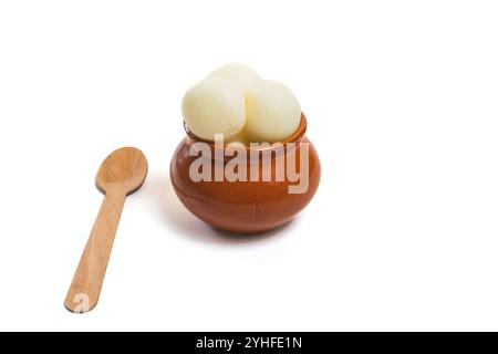 Ein traditionelles indisches Dessert, Rasgulla, serviert in einem rustikalen Tontopf mit einem Holzlöffel, isoliert auf weißem Hintergrund. Stockfoto