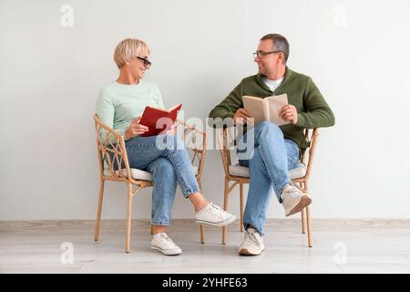 Ein älteres Paar sitzt in Sesseln und liest Bücher in der Nähe der weißen Wand Stockfoto