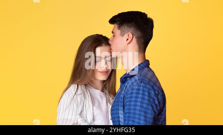 Der Kerl küsst Dame auf der Stirn auf gelbem Hintergrund Stockfoto