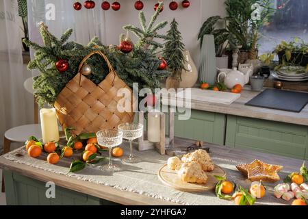 Eine gemütliche Küche für Familienurlaub, mit einem Korb gefüllt mit Tannenzweigen und roten Ornamenten. Der Tisch ist mit Mandarinen dekoriert, Stockfoto