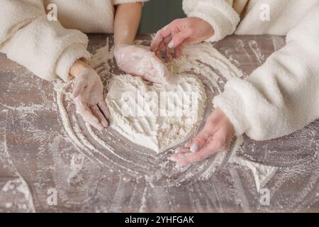 Weibliche Hände von Mutter und Tochter machten ein Herz aus Mehl auf dem Tisch, Blick von oben, Familienglück Konzept Stockfoto