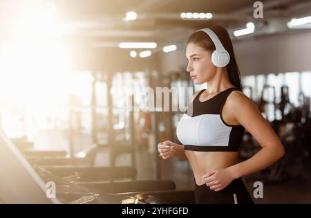 Sport und Workout. Junge Frau mit Kopfhörern, die im Fitnessstudio Laufband benutzt Stockfoto