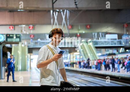 latino Mann wartet auf einem Bahnsteig mit seinem Smartphone Stockfoto