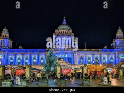 Belfast, Großbritannien, 18. Dezember 2023. Der Straßenblick auf die Vorderseite des Belfast Rathauses Weihnachtsmarkt mit farbenfrohen Lichtern am Abend. Stockfoto