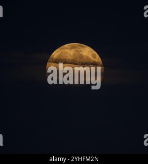 Der Mond, der tief am Horizont aufsteigt, mit Wolken darüber und erzeugt einen gruseligen Effekt mit Kopierraum. Stockfoto