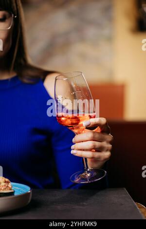 Nahaufnahme einer Frauenhand, die ein Glas Rosenwein hält und Eleganz und Entspannung zeigt Stockfoto