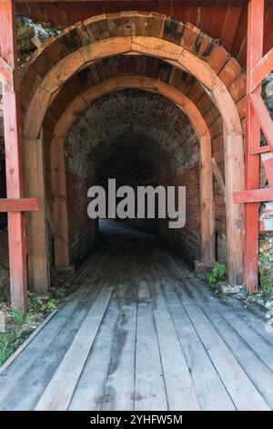 Ein bogenförmiger Eingang führt in einen dunklen Tunnel, der aus Holz und Stein in einer historischen Festung gebaut wurde. Der schwache Durchgang weckt ein Gefühl von Mysterium Stockfoto