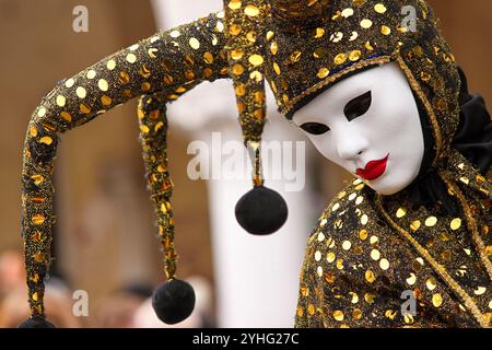 Eine Nahaufnahme eines maskierten Darstellers beim venezianischen Karneval, der ein glitzerndes Gold-schwarzes Narrenkostüm trägt. Stockfoto