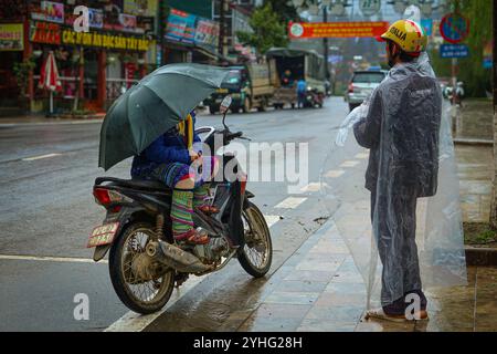 Ein Motorradfahrer mit Regenschirm und ein anderer in einem Regenponcho, der an einem regnerischen Tag in Vietnam auf einer nassen Straße stand. Stockfoto