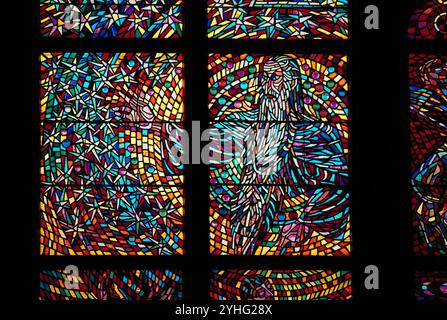Eine Nahaufnahme eines bunten Buntglasfensters, das abstrakte religiöse Bilder in leuchtenden Rot-, Blau-, Gelb- und Violetttönen zeigt. Stockfoto