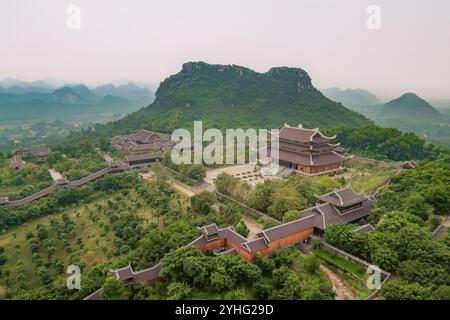 Blick aus der Vogelperspektive auf den Bai Dinh Temple Komplex, umgeben von üppigem Grün und Bergen in Ninh Binh, Vietnam. Das weitläufige Tempelgelände verschmilzt mit der Natur. Stockfoto