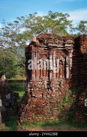 Altes gemeißeltes Steinrelief auf verwitterter Tempelmauer, teilweise mit Moos bewachsen, inmitten einer üppigen, grünen Landschaft. Stockfoto