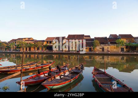 Ein malerischer Blick auf Hoi ans Ufer bei Sonnenaufgang mit traditionellen Holzbooten, die auf dem ruhigen Fluss schwimmen. Stockfoto