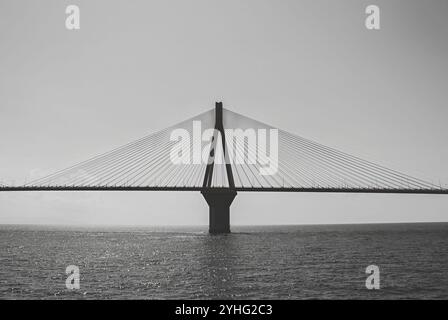 Schwarz-weiß-Bild einer Hängebrücke über ruhigem Wasser, die die schlanken architektonischen Linien vor einem minimalistischen Himmel zeigt. Stockfoto