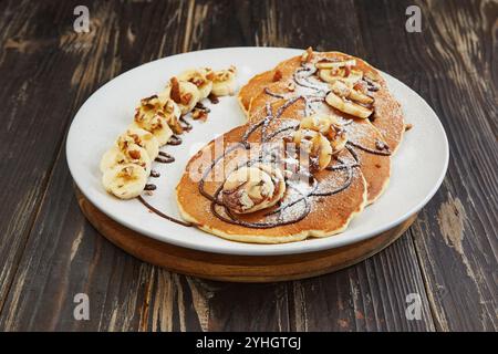 Köstliche Pfannkuchen mit geschnittenen Bananen, gehackten Nüssen und Schokoladennebel, die ein köstliches und optisch ansprechendes Frühstücksgericht schaffen. Stockfoto