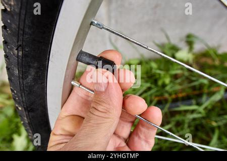 Die Kappe des Fahrradreifens wird mit den Fingern des Radfahrers entfernt, bevor der Schlauch mit Luft aufgepumpt wird. Stockfoto