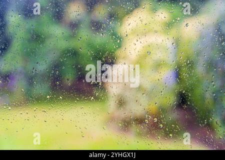 Regen fällt auf ein Fenster mit Grün aus einem unscharfen Garten dahinter, die Darstellung des Klimawandels Stockfoto