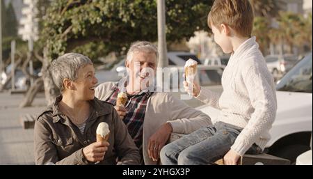 Großeltern, Enkel und Essen Eis draußen auf dem Parkplatz für Nachtisch, süße Snacks und Bonding. Senioren, glückliches Kind und entspannen Sie sich Stockfoto
