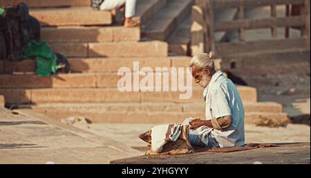 Varanasi, Indien. Der Alte Bettler Zählt Seine Einnahmen. Ein Alter Mann Sitzt Am Ganges Embankment. Der Senior-Mann Zählt Sein Geld. Vormittag Im Heiligen Varanasi Ghats Stockfoto