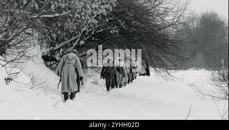 Männer, die als Soldaten der Weißen Garde der kaiserlichen russischen Armee im russischen Bürgerkrieg gekleidet sind, marschieren durch den verschneiten Winterwald. Armee auf dem Marsch. Historisch Stockfoto