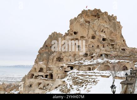 UCHISAR, NEVSEHIR, TÜRKEI - 4. FEBRUAR 2017: Ruinen der Festung Uchisar mit türkischer Flagge und schneebem Berg im Hintergrund Stockfoto