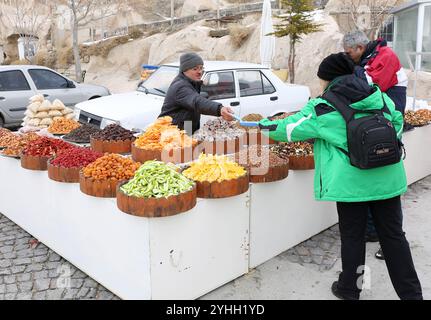 UCHISAR, NEVSEHIR, TÜRKEI-04. FEBRUAR 2017: Unbekannter Verkäufer von getrockneten Früchten gibt an einem kalten Wintertag Proben an Touristen Stockfoto