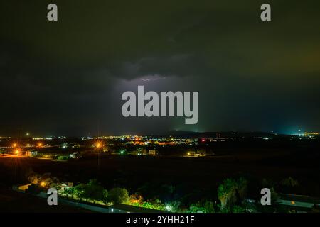 Leuchtende Blitze über dem Nachthimmel über der ruhigen Stadt enthüllen verborgene Landschaften. Stockfoto
