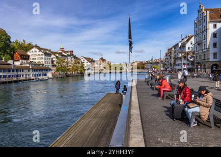 Stadt Zürich an der Limmat in der Schweiz. Die Gäste befinden sich auf der Terrasse am Fluss mit Bänken im Stadtzentrum, Teil der Altstadt. Stockfoto