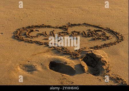 Die herzförmige Inschrift im Sand fängt einen Moment an einem ruhigen Strand bei Sonnenuntergang ein. Stockfoto