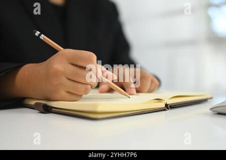 Nahaufnahme einer Geschäftsfrau, die mit einem Bleistift Notizen im Tagebuch macht Stockfoto