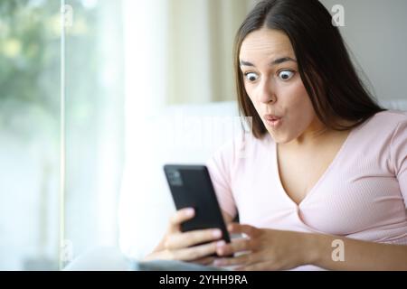 Überraschte Frau, die zu Hause Online-Inhalte von Mobiltelefonen ansieht Stockfoto