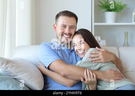 Glückliches Paar zu Hause, das auf einer Couch sitzt und dich ansieht Stockfoto