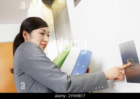 Frau im Anzug, die den Aufzug mit vielen Papieren drückt Stockfoto