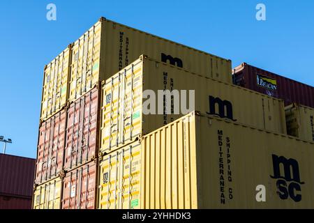 Frachtcontainer der msc mediterranean Reederei stapelten sich hoch in einer Werft unter einem klaren blauen Himmel und symbolisieren den globalen Handel und die Logistik Stockfoto