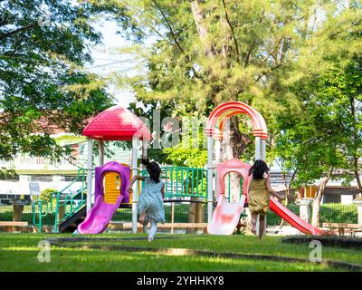 Niedliche Schwestern, die Spaß auf einer bunten Rutsche in einem Outdoor Park haben. Kinder spielen während der Sommerferien auf dem Spielplatz. Stockfoto