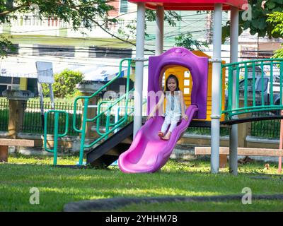 Niedliches Mädchen, das Spaß auf einer bunten Rutsche in einem Outdoor Park hat. Kinder spielen während der Sommerferien auf dem Spielplatz. Stockfoto