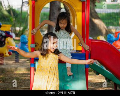 Niedliche Schwestern, die Spaß auf einer bunten Rutsche in einem Outdoor Park haben. Kinder spielen während der Sommerferien auf dem Spielplatz. Stockfoto