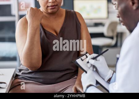 Abgeschnittene Aufnahme einer erwachsenen Afroamerikanerin, die mit dem Arzt in der Klinik spricht und Hautausschlag auf den Armen zeigt Stockfoto